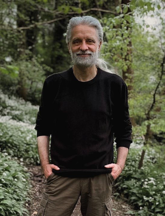 Portrait of counsellor Richard Warden standing on a woodland path, smiling warmly. 